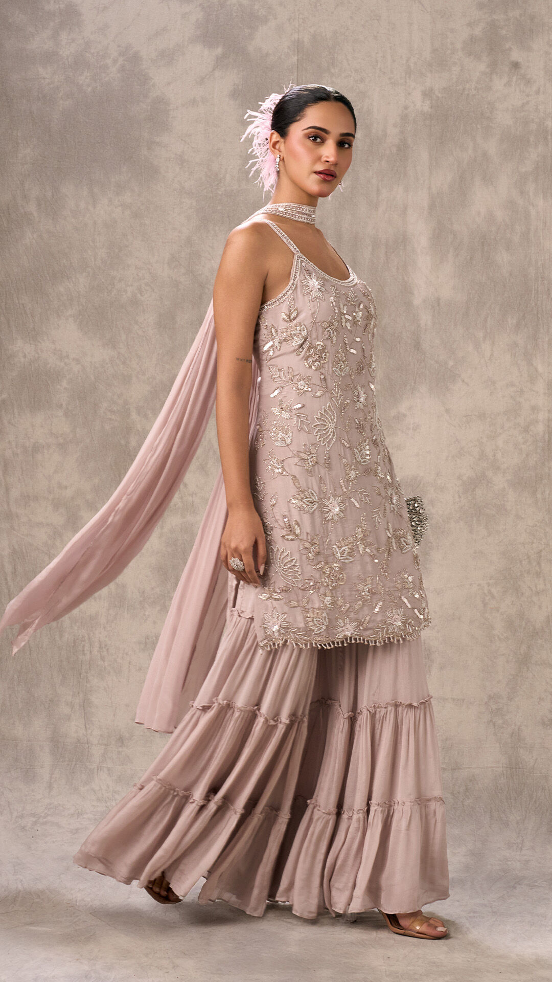 Woman in a heavily embroidered light pink Gharara suit with a sheer dupatta, showcasing an intricate festive outfit.